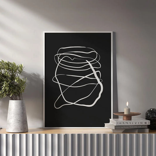 Plakat z czarno-białą, abstrakcyjną grafiką w stylu swobodnego szkicu wykonanego jedną linią wiszący w salonie