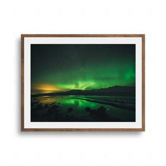 Plakat przedstawiający zieloną zorzę polarną nad ciemnym krajobrazem, odbijającą się w tafli wody.