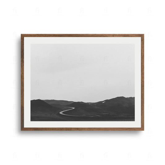 Czarno-białe zdjęcie pustej, krętej drogi prowadzącej przez surowe pustkowie z jasnym niebem