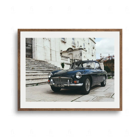 Plakat ze zdjęciem ciemnego, klasycznego samochodu sportowego kabriolet zaparkowanego przed eleganckim budynkiem z kamiennymi schodami.